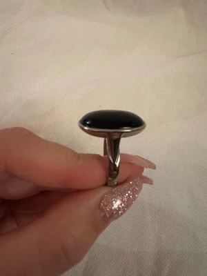 Stor silverring med svart oval sten - Säljer en chunky silverring med en stor, oval svart sten som mäter ca 2 cm. Ringen har en stilren och modern design med blank yta och bred ring. Perfekt statement piece för dig som gillar att sticka ut med dina accessoarer.