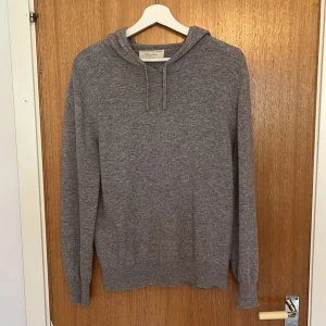 Grå kashmirhoodie från Sayless - Mjuk och stilren grå hoodie från Sayless i lyxig kashmir. Tröjan har huva med snörning och långa ärmar, perfekt för dig som gillar en chill och clean look. Passar dig som vill ha något både bekvämt och snyggt till vardags.