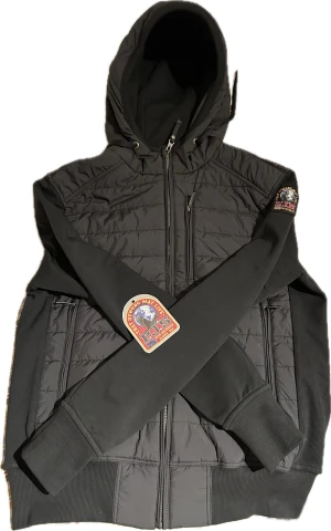 Parajumpers cardigan  - Exklusiv svart cardigan från Parajumpers – en perfekt mix av funktion och stil. Tillverkad i högkvalitativa material med stretch, dragkedja och klassisk Parajumpers-logo på ärmen. Snygg att bära som jacka under höst/vår eller som mellanlager under kallare dagar. En mångsidig och stilren investering! Välvårdad och redo att bäras direkt!