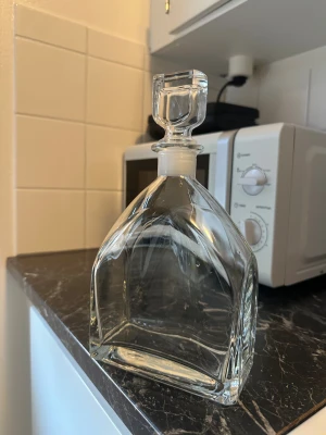 Glasdekanter med propp - Elegant glasdekanter med modern design och fyrkantig propp. Perfekt för servering av whisky, vin eller sprit. Dekantern är i mycket gott skick utan synliga repor eller skador. Passar både till fest och vardag. Rymmer generös mängd dryck och är lätt att rengöra.