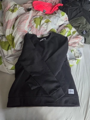 Svart sweatshirt från Andy by Frank Dandy - Svart sweatshirt från Andy by Frank Dandy i storlek L. Tröjan har en klassisk rund halsringning, ribbade muddar och en stilren look utan mönster eller detaljer. Perfekt för dig som gillar enkel och clean stil.