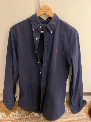 Mörkblå skjorta från Polo Ralph Lauren - Klassisk mörkblå skjorta från Polo Ralph Lauren med röd broderad logga på bröstet. strl M funkar som L