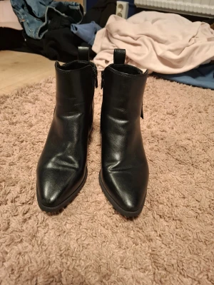 Svarta stövletter med klack och dragkedja - Snygga svarta stövletter i skinnimitation med spetsig tå och låg klack. Guldiga dragkedjor på sidan ger en extra touch. Perfekta till jeans eller kjol när du vill ha en stilren look. Köpte för ca 400 och nästan aldrig använda