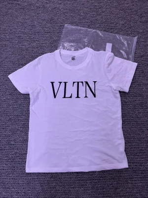 Vit Valentino t-shirt i bomull - Vit t-shirt från Valentino med VLTN-tryck i svart på bröstet. Klassisk rund hals och korta ärmar. Tillverkad i mjuk bomull som känns skön mot huden. Enkel och stilren design som funkar till många olika looks.