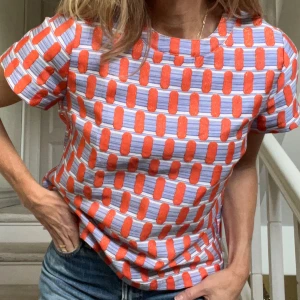 Fantastisk topp från Coster Copenhagen - Unik och fräsch topp från Coster Copenhagen med kort ärm och rak passform. Lite styvt tyg med inslag av glitter i orange partier mot blå och vit bakgrund - perfekta färgkombinationer. Snygg dragkedja baktill. Styla till vita byxor eller jeans på vår/sommar - piggar också upp till svart på vinterhalvåret. Dansk kvalitet och design som håller länge. 