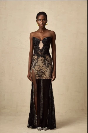 Svart spetsklänning med slits - Supersnygg långklänning i svart spets med nude underklänning. Klänningen är axelbandslös och har en djup v-ringning med transparent meshdetalj framtill. Den har en hög slits på ena sidan och glittriga paljetter i spetsen för extra wow-effekt. Perfekt för bal eller fest! Aldrig använd då den kom 1 vecka försent, den har  prislapp kvar, köpte den för 2679kr på rea, klänningen kommer även med handskar, vill ni ha bilder så tveka inte och höra av er💕💕