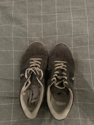 Gråa sneakers från Polo Ralph Lauren - Snygga bruna sneakers från Polo Ralph Lauren med klassisk design och beige snörning. Skorna har rund tå och är tillverkade i mocka med diskret logga på sidan. Perfekta för dig som gillar stilrena och tidlösa sneakers.