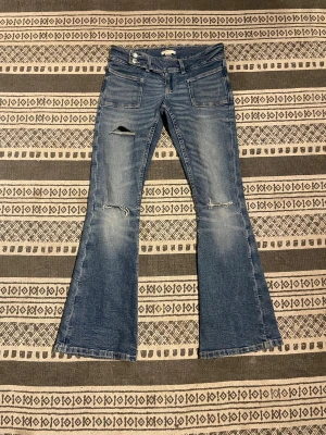 Blå bootcut jeans med slitningar - Snygga blå jeans med bootcut passform och slitna detaljer vid knäna. Jeansen han en låg midja och en blå färg. Mycket stretchigt material med snygga detaljer. Från Ginatricot 💓