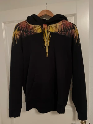 Svart hoodie med färgglada fjädrar - Svart hoodie från Marcelo Burlon köpt i Farfetch 