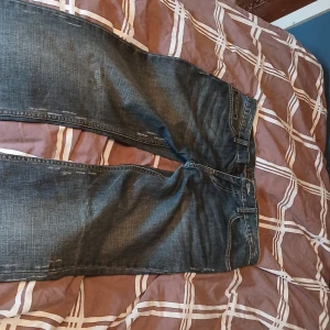 Mörkblå low waist jeans 2000s stil - Snygga mörkblå jeans med raka ben och diskreta slitningar. Klassisk femficksmodell med kontrastsömmar och bälteshällor. Jeansen har en något tvättad look och är tillverkade i robust denim för en cool vardagsstil. W30L32 passar str 36