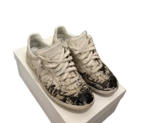 Maison Margiela - Unika Maison Margiela sneakers i vitt med coola svarta färgstänk. Skorna har en klassisk snörning och är i bra skick trots den avsiktliga slitna looken. Perfekta för dig som vill sticka ut med en grisch stil! Buda gärna och tar även emot byten!!