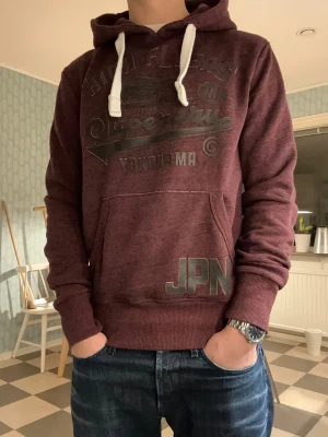 Superdry JPN hoodie - En vinröd, stilren och snygg superdry hoodie! Storlek S(står xs på lappen, men passar definitivt som S). Bra passform och passar perfekt till ett par mörkare jeans😮‍💨 Är i nyskick med inga defekter, ser ut som direkt ur fabrik🤩Var som vanligt inte rädda att skicka prisförslag eller frågor!
