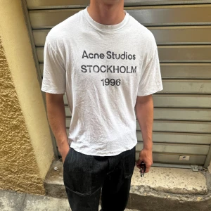 Vit Acne Studios t-shirt - Säljer en vit t-shirt från Acne Studios med svart texttryck 'STOCKHOLM 1996' på bröstet. Size XS men sitter som S-M. Modellen är klassisk med rund hals och korta ärmar, och har en loose passform. Materialet är mjuk bomull som känns skönt mot huden.
