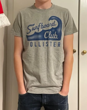Grå t-shirt Hollister Surfboard Club - Grå T-Shirt från Hollister | Storlek Small men passar som Small/Medium | Mycket bra skick | Modellen på bilden är 173cm
