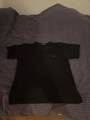 Svart t-shirt från Acne Studios - Säljer en svart t-shirt från Acne Studios med klassisk passform och diskret logopatch på bröstet. T-shirten har rund halsringning och är tillverkad i mjuk bomull, perfekt för en clean och stilren look.