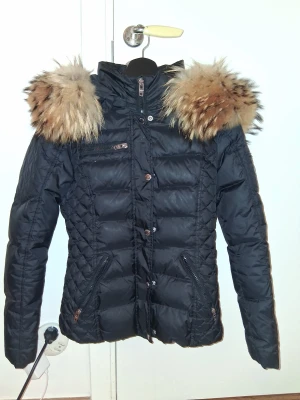 Rockandblue strl 32 - Snygg svart dunjacka från Rockandblue med stor fluffig päls i beige/brun runt kragen. Jackan är i mycket bra skick. Perfekt till kallare tider. ❤️