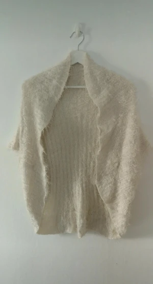 Vit lätt fluffig kofta - Supermjuk och fluffig vit kofta utan ärmar. Koftan är stickad och har en öppen front med bred krage.