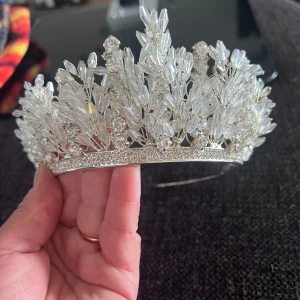 Glittrigt diadem med kristaller - Säljer ett riktigt snyggt diadem med massor av glittrande kristaller och pärlliknande detaljer i silver. Diademet har en lyxig och unik design som verkligen sticker ut och ger en kunglig vibe. Perfekt för att maxa din look med extra bling och elegans.