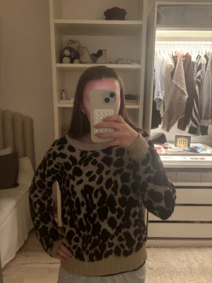 Beige leopardmönstrad stickad tröja - Säljer en beige stickad tröja med svart leopardmönster. Tröjan har rund halsringning, ribbade muddar och är långärmad. Perfekt för dig som vill sticka ut lite extra med ett djurmönster i garderoben.