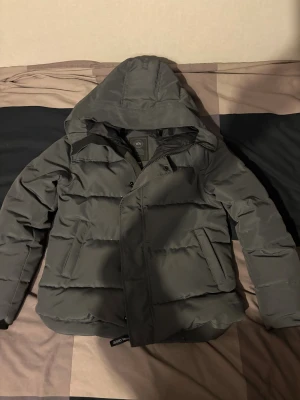 Svart pufferjacka från Canada Goose - Säljer en svart pufferjacka från Canada Goose med huva och diskret svart logotyp på ärmen. Jackan har dragkedja och knappar framtill, två stora fickor och quiltad design. Perfekt för kalla dagar och riktigt snygg till streetwear-stilen. Stolek m, passar även stolek S pris kan diskuteras 