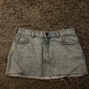 Ljusblå jeanskjol med rå kant - Säljer en ljusblå jeanskjol med klassisk femficksdesign och rå, fransig kant nedtill. Kjolen har bälteshällor, knapp och dragkedja framtill samt två stora bakfickor. Den är även lågmidjad i modellen. Perfekt för dig som gillar en bra denomlook. Den är köpt på plick men aldrig använd sen dess. Liten i storleken.