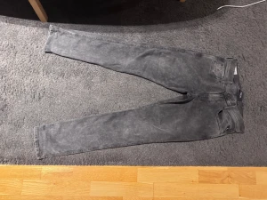 Replay anbass jeans - Snygga grå jeans från Replay med tvättad look och klassisk femficksdesign. Modellen är skinny med smal passform och raka ben, perfekt för dig som gillar en modern stil. Jeansen har dragkedja och knapp i midjan samt detaljerade bakfickor.