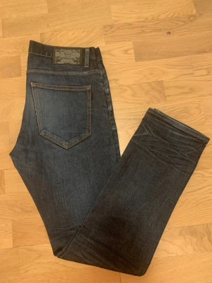 Mörkblå Crocker jeans straight fit - Snygga mörkblå jeans från Crocker med klassisk femficksdesign och kontrastsömmar. Modellen har rak passform och normal midja, tillverkade i slitstark denim med diskret tvättad look. Perfekt för dig som gillar tidlös stil och enkelhet. Det finns ett slit men inte hål som ni kan se den på bilden 
