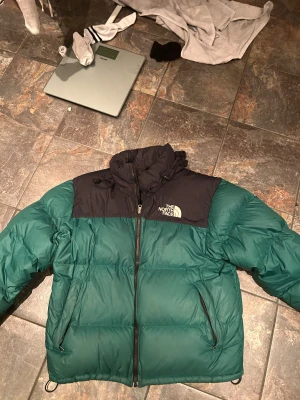  The North Face jacka  - Säljer en fet dunjacka från The North Face i grön och svart. Jackan har hög krage, två sidofickor med dragkedja och logga på bröstet och ryggen. Perfekt för kalla dagar, med riktigt puffig look och snygg färgkombination.