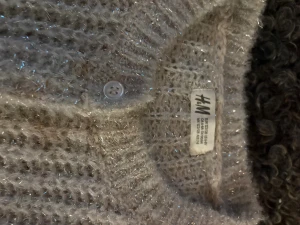 Glittrig grå kofta från H&M - Säljer en grå glittrig kofta från H&M i storlek 122/128. Koftan är stickad med ett fluffigt material och har knappar framtill. Perfekt för dig som gillar lite extra shimmer i vardagen. Långärmad och supermysig att ha på sig.
