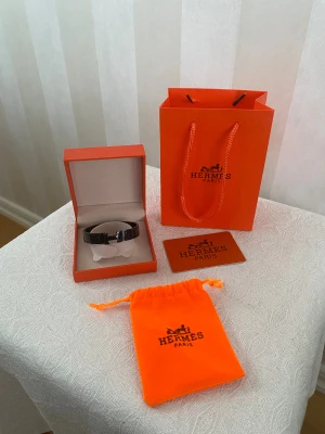 Hermes armband svart  - Snyggt svart armband från Hermès med klassisk H-detalj i metall. Kommer med original ask, påse och certifikat. Armbandet har en stilren och modern design som passar perfekt till dig som gillar exklusiva accessoarer och vill sticka ut med något från ett ikoniskt märke.
