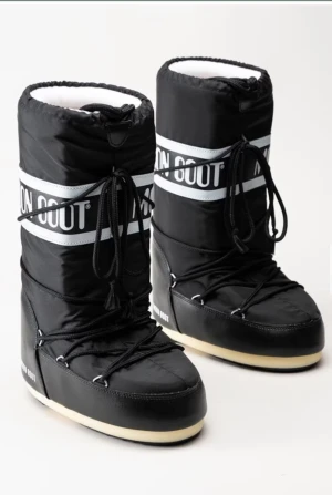 Svarta Moon Boots med snörning - Moon Boots i svart med vit logga och snörning runt skaftet. Höga och vadderade med platt sula och rund tå. Utsidan är i syntetmaterial och insidan är fodrad för extra värme. Använda två gånger, original pris 2200