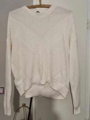 Vit stickad tröja med strukturmönster - Säljer en vit stickad tröja med snyggt strukturmönster framtill och ribbade muddar vid ärmslut och nederkant. Tröjan har rund hals och lång ärm, perfekt för dig som gillar en enkel men ändå cool look. Passar dig som vill ha en mysig och stilren vibe.