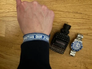 Blå Christian Dior J'Adior armband - Snyggt blått tygarmband från Christian Dior med vit text 'J'Adior'. Armbandet har en justerbar knytning och är tillverkat i ett slitstarkt textilmaterial. Perfekt accessoar för dig som gillar designer och vill sticka ut med en cool detalj på handleden.