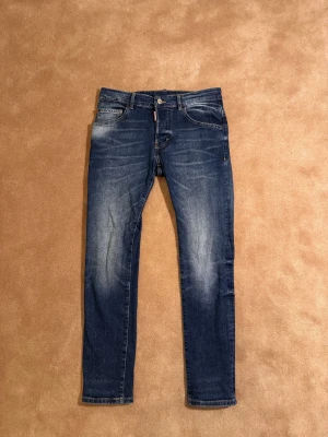 Dsquared2, storlek 16Y/42 - Snygga blå jeans från Dsquared2 med klassisk femficksdesign och coolt tryck på bakfickan. Skick= 9/10. Nypris 3999kr , Säljes för 399kr. Modellen har har orginalslitningsr från fabrik vilket är eftertraktat och populärt. 