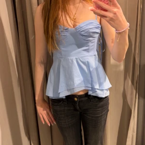 Ljusblå  topp med volang - Supersöt ljusblå topp topp med smala axelband och volang nedtill. Toppen har en snygg v-ringning och lätt rynkade detaljer vid bysten. 