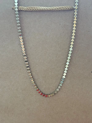 Guldigt halsband med hjärtan - Unikt halsband i guldfärgad metall med små hjärtformade länkar. Några av hjärtana är målade i rött och rosa vilket ger en cool detalj. Kedjan är smal och har ett klassiskt lås. Perfekt för dig som gillar smycken med lite extra personlighet.