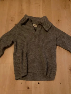 Grå ribbad stickad tröja Object - Säljer en grå stickad tröja från Object i storlek S. Tröjan har en bred krage, v-ringning och en snygg half zip-dragkedja framtill. Ribbad struktur och långa ärmar gör den perfekt för kyliga dagar. Enkel att styla med jeans eller kjol.