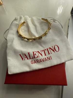 Valentino armband - Valentino Garavani Rockstud-armband i guldtonad metall. Använd en del och har enstaka defekter vilket man ser på tredje bilden. Ikoniskt och stilrent smycke, kommer med originalpåse och ask. Köpt på MyTheresa för 6000kr.