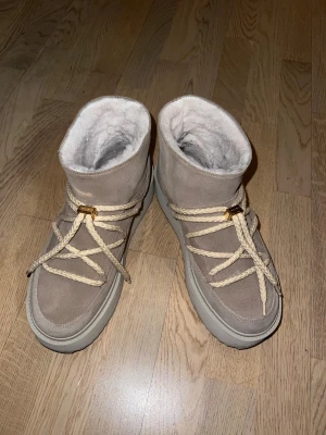 INUIKII Boots Classic Low Platform - Säljer ett par beige INUIKII Boots Classic Low Platform. Skorna har mockayta och rejäla, krämfärgade snören med gulddetaljer. Perfekta för kalla dagar när du vill hålla stilen och värmen.
