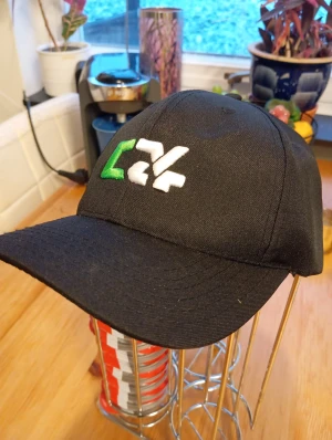 Ny keps med broderad logga - Ny keps med böjd skärm och broderad logga i vitt och grönt framtill. Snygg och enkel design som passar till de flesta outfits. Tillverkad i ett slitstarkt tyg med klassisk passform och justerbar baksida.