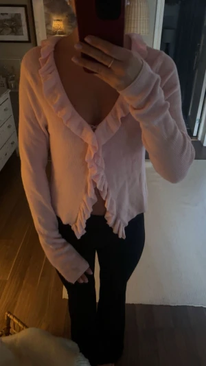 Ljusrosa kofta med volangkant - Superfin ljusrosa kofta med volang längs hela kanten och v-ringad hals. Tröjan är ribbad och har långa ärmar, perfekt för dig som gillar söta detaljer och mjuka färger. Ej använd! 