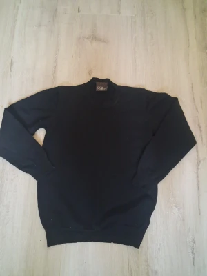 Svart polotröja från Oscar Jacobson - Svart polotröja från Oscar Jacobson i storlek M. Tröjan har en klassisk hög krage och är långärmad, perfekt för att hålla värmen under kyliga dagar. Materialet är mjukt och stickat, vilket gör den skön att bära och enkel att matcha med andra plagg.
