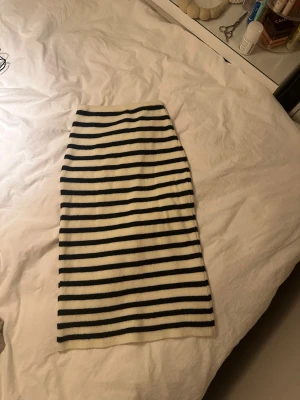 Randig ribbad kjol i svart och vitt - Säljer en snygg ribbad kjol med svarta och vita horisontella ränder. Kjolen är midilång och har en rak passform som sitter skönt på kroppen. Perfekt för dig som gillar en stilren och trendig look. Aldrig använd!
