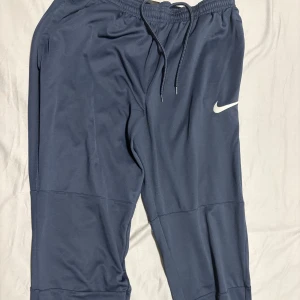 Nike Dri-Fit blå mjukisbyxor M - Blå mjukisbyxor från Nike med Dri-Fit-teknologi, perfekt för träning. Byxorna har snörning i midjan, elastisk linning och ribbade muddar vid bensluten. Swoosh-logga på benet och praktiska sidofickor. Sköna och sportiga med loose passform.(aldrig använt, hann aldrig komma till användning) köptes för 800kr drf ärde lägsta 400kr.