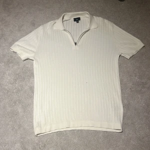 Ribbad beige pikétröja med dragkedja - Snygg ribbad pikétröja från H&M i beige med korta ärmar och krage. Tröjan har en stilren half zip-dragkedja framtill och är tillverkad i mjukt material som känns skönt mot huden. Perfekt för en clean och modern look.