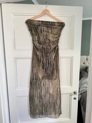 Lång meshklänning med zebramönster - Säljer en lång, axelbandslös meshklänning med transparent tyg och zebrainspirerat mönster i grön, beige och bruna toner. Klänningen har en figurnära passform och är perfekt för dig som vill sticka ut med en edgy look.