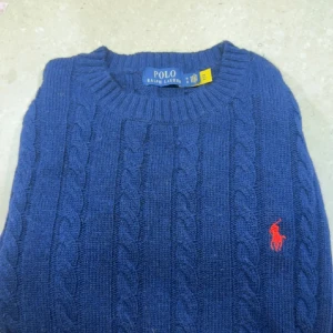 Blå kabelstickad tröja Polo Ralph Lauren - Kabelstickad blå tröja från Polo Ralph Lauren med klassisk rund hals och röd broderad logga på bröstet. Tröjan har långa ärmar och ribbade muddar vid ärmslut och nederkant. Riktigt fräsch använt väldigt få gånger. Pris går o diskutera:) Nypris: 1799kr, mitt pris 699kr🤩