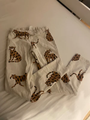 Beige leggings med leopardmönster Lindex - Snygga beige leggings från Lindex med coolt leopardmönster i brunt och svart. Mjukt bomullsmaterial och elastisk midja för skön passform. Perfekt för dig som gillar djurprint och vill sticka ut lite extra. Barn till tjejer storlek 128