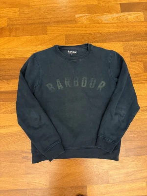 Mörkblå sweatshirt från Barbour S - Snygg mörkblå sweatshirt från Barbour i storlek M men fittar som S. Tröjan har rund hals, långa ärmar och ett stort Barbour-tryck framtill. Tillverkad i mjuk bomullsmix som är skön mot huden. Perfekt för dig som gillar klassisk och enkel stil.