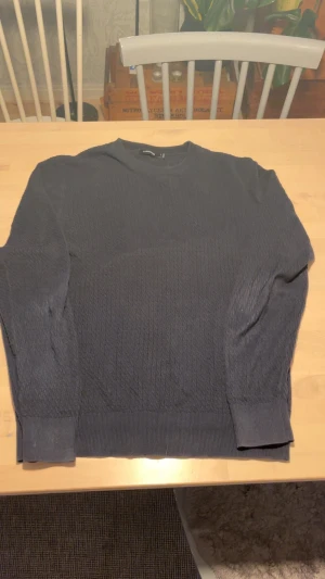 Mörkblå stickad tröja J.Lindeberg M - Mörkblå stickad tröja från J.Lindeberg i storlek M. Tröjan har ett diskret mönster, rund halsringning och ribbade muddar vid ärmslut och nederkant. Perfekt för dig som gillar stilrena och klassiska plagg med en modern touch.